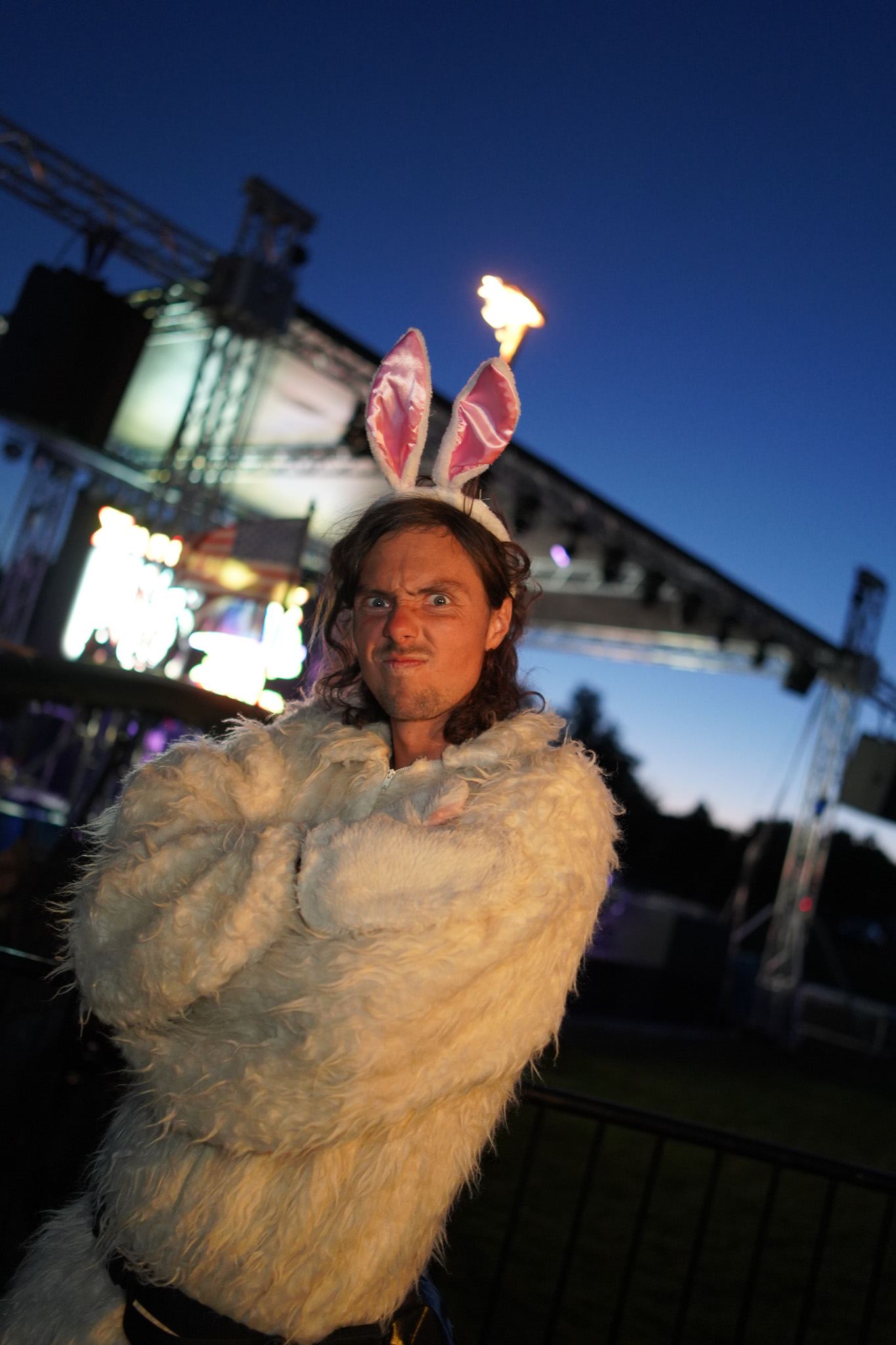 Bass Bunny in bunny ears and a white fur coat in front of the stage at dusk