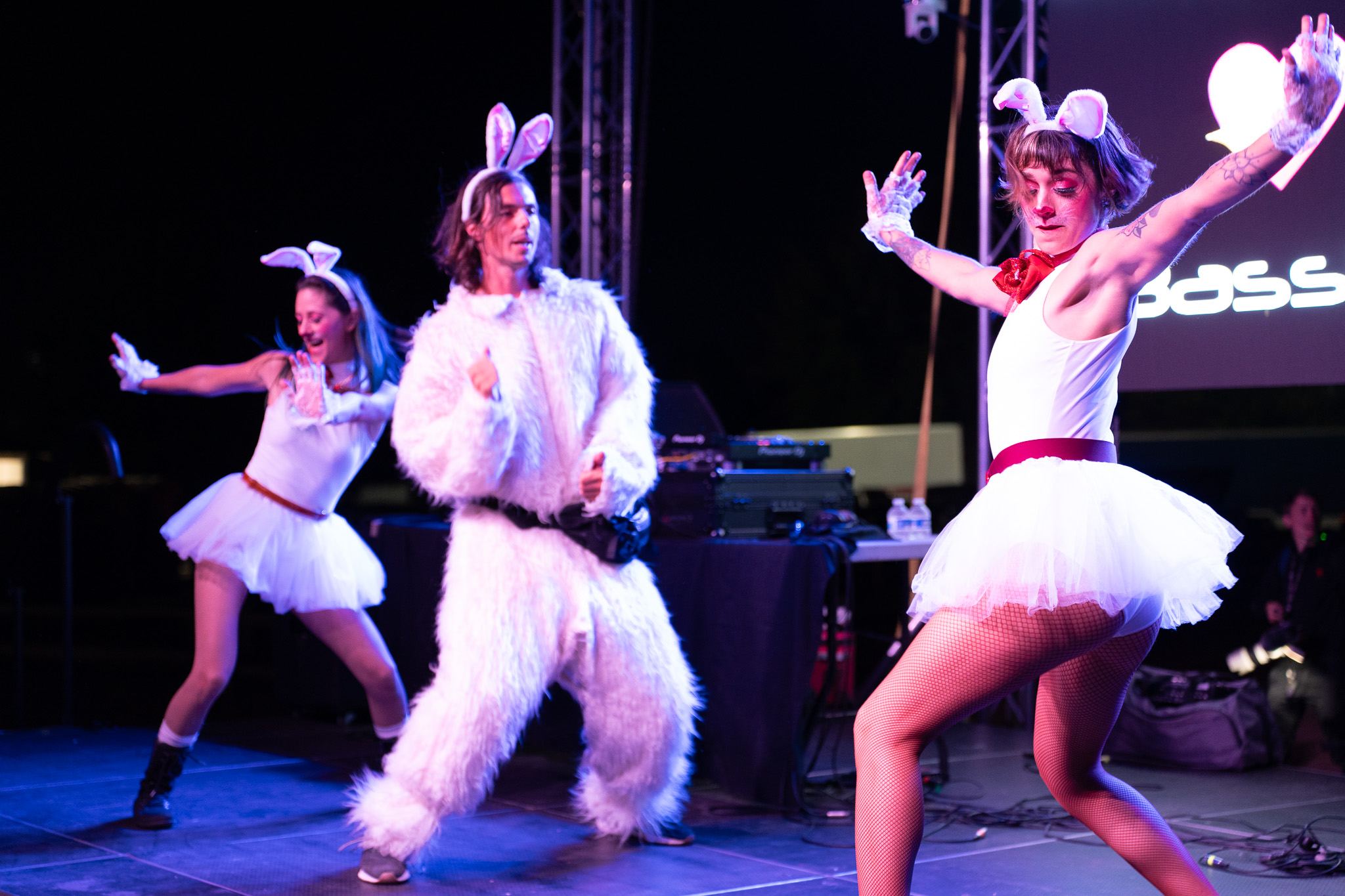 Bass Bunny dancing on stage in a white bunny suit with two dancers in bunny ears and tutus