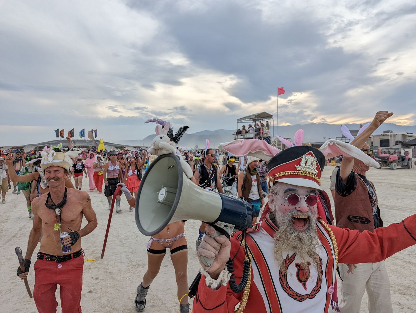 A marcher in a red band uniform shouting into a megaphone among people in bunny ears on the playa