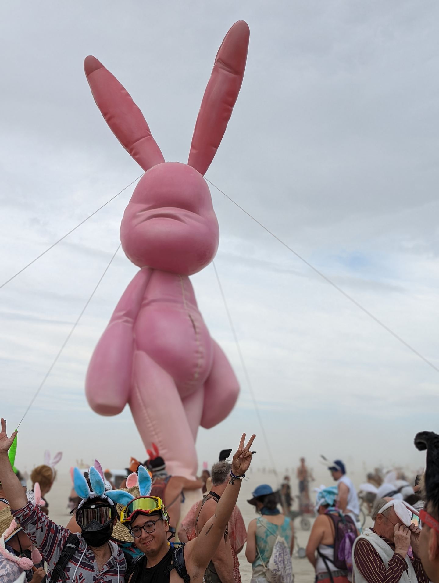 A giant pink inflatable bunny floating above a crowd wearing bunny ears